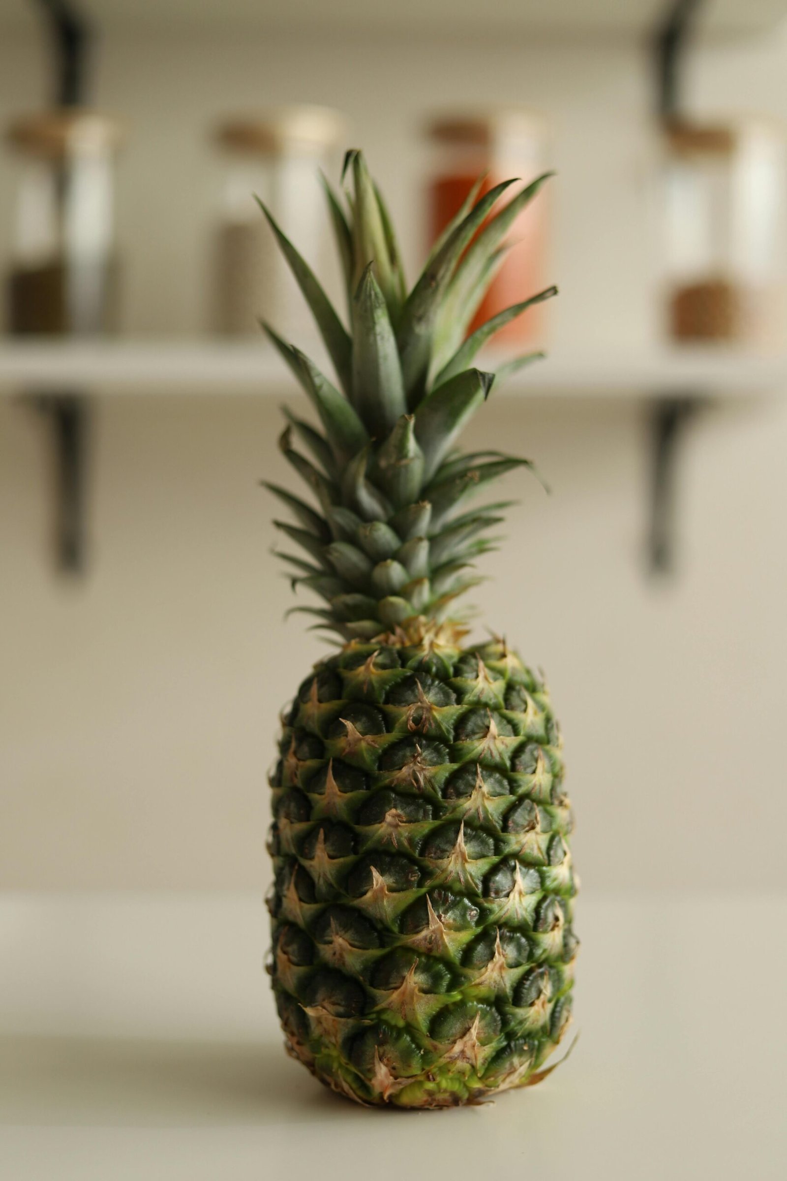 A vibrant pineapple stands in focus on a kitchen counter with spices in the background.