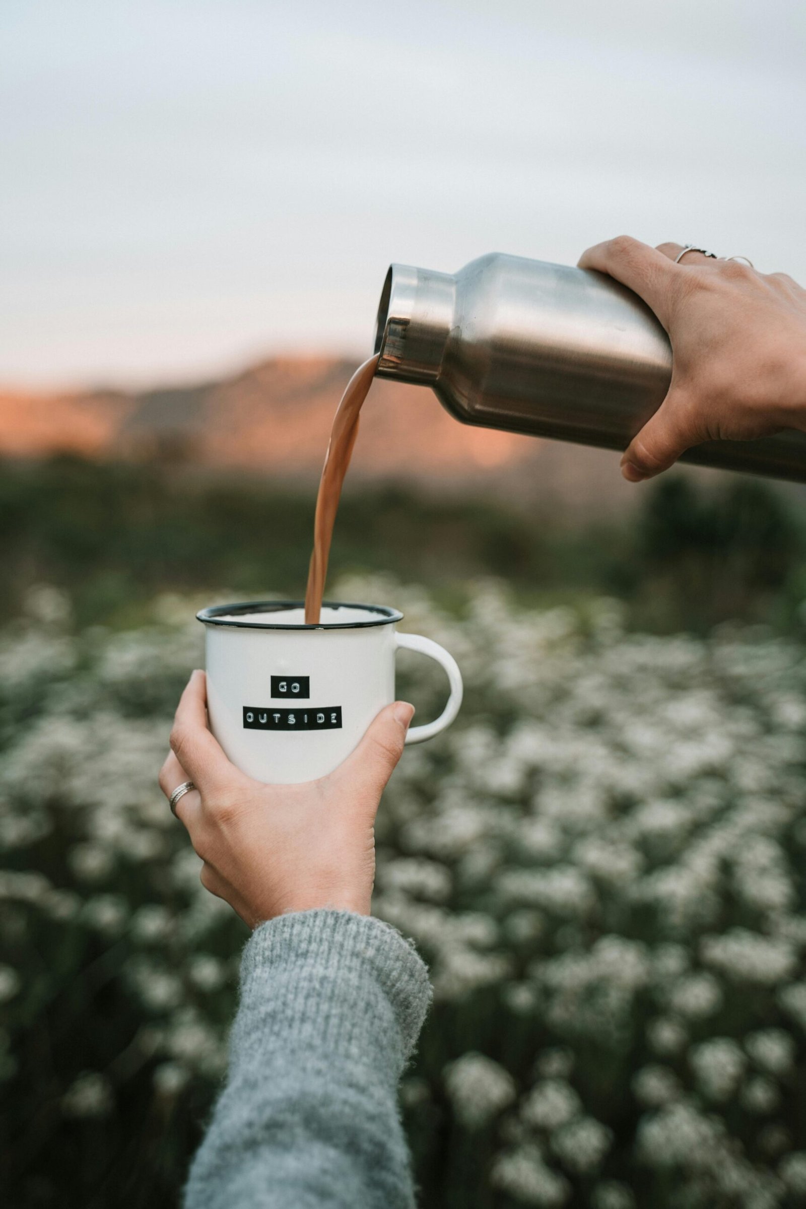 Hands pouring coffee into a mug in beautiful outdoor setting, inspiring adventure.